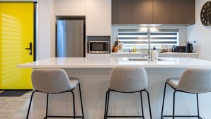 A modern kitchen with a central island, bar stools, a microwave, and a stainless steel refrigerator. - Urban comfort and parking near Avebury Park (Christchurch)