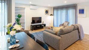 A modern living room with a grey sofa, a TV, and a dining table with a vase of flowers. - Urban comfort and parking near Avebury Park (Christchurch)