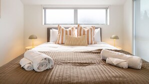 Una cama bien hecha con almohadones a rayas, una toalla enrollada y una colcha marrón acolchada.