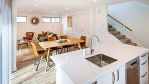 Una cocina moderna con armarios blancos, una isla central con un lavamanos y una zona de comedor con una mesa y sillas de madera.