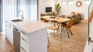 Una cocina moderna con una isla central, un comedor con sillas de madera, un sofá y un televisor al fondo.