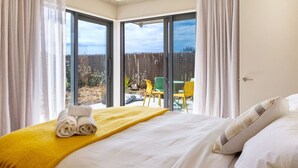 A hotel room with a bed, a yellow blanket, and a view of an outdoor area with chairs and a fence. - The Keep - Waimairi Beach (Christchurch)