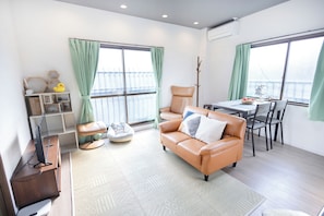 A modern living room with a leather sofa, a dining table, and a large window with curtains.
