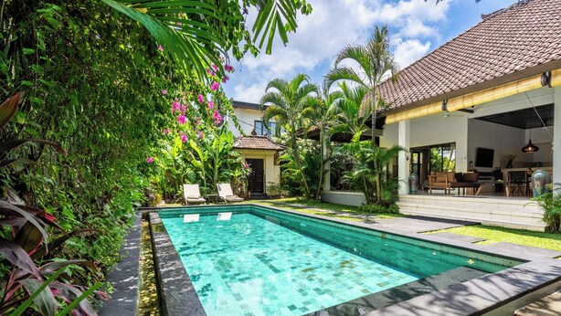 A swimming pool surrounded by lush greenery, a covered outdoor seating area, and a building with a tiled roof. - Villa Amaro - 2 Bedrooms (Seminyak)