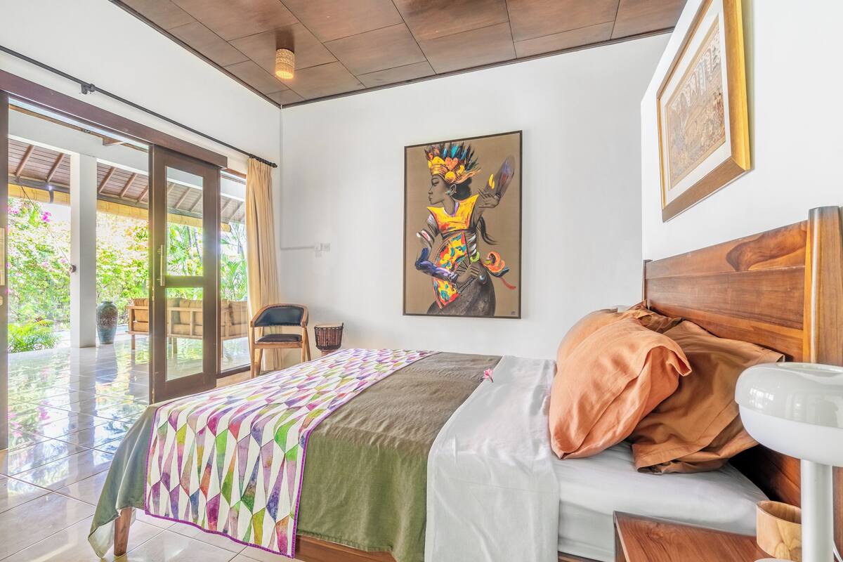 Une chambre d’hôtel avec un lit, une tête de lit en bois, un tableau au mur et une vue à travers la porte vitrée.