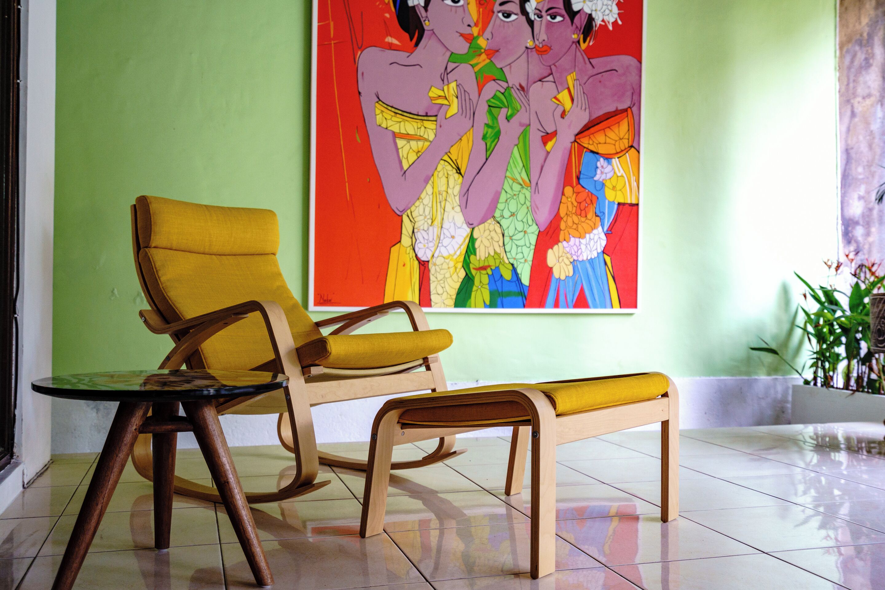 A room with a wooden chair and bench, a green wall, and a colorful painting.