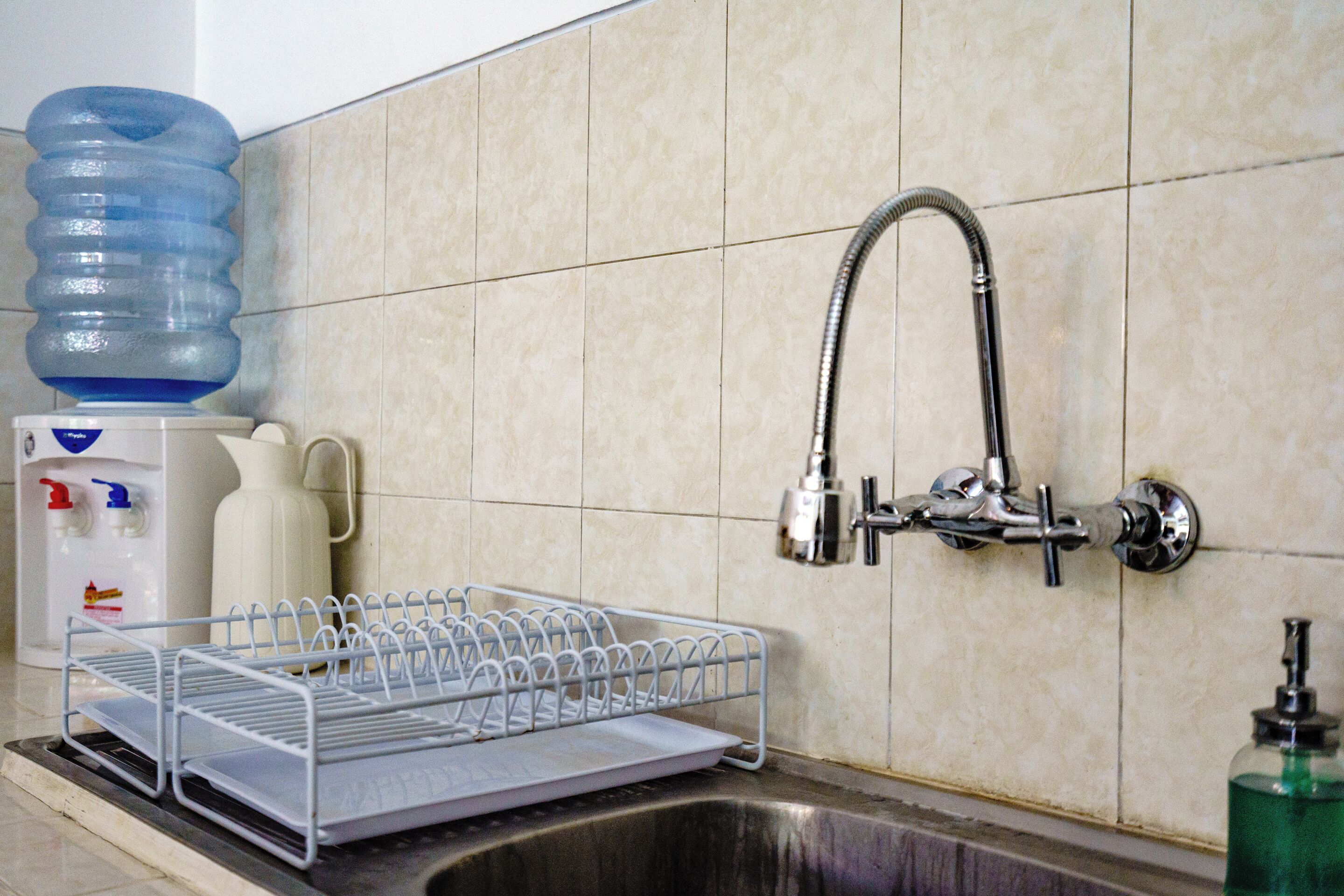 A kitchen with a stainless steel sink, a dish drying rack, a water dispenser, and a soap dispenser.