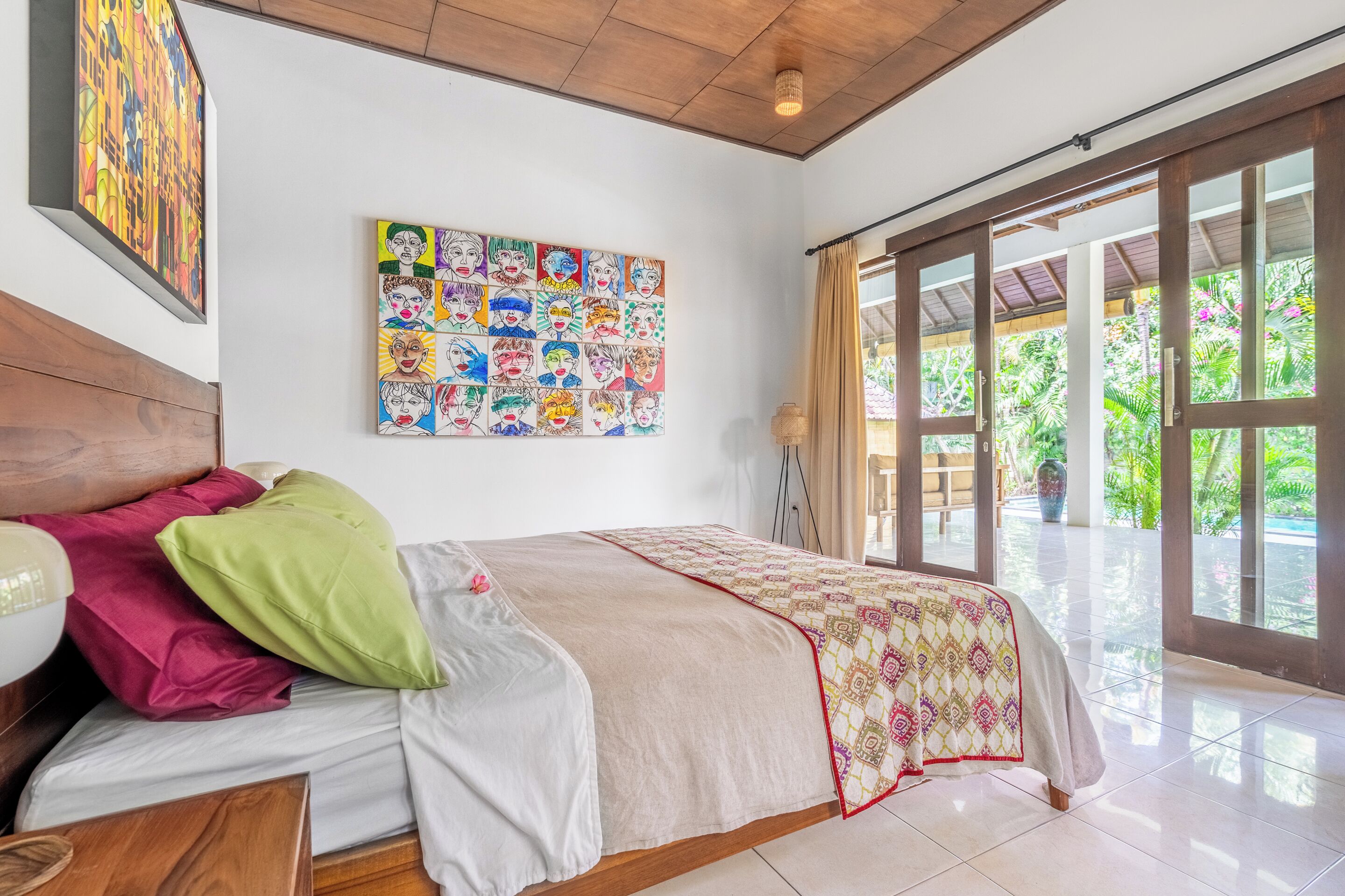 Camera da letto con un letto grande, una testiera in legno, un'opera d'arte colorata al muro e vista su piante verdi.