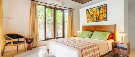 Un dormitorio con una cama, una silla, un tambor, una mesita de noche y una ventana con cortinas.