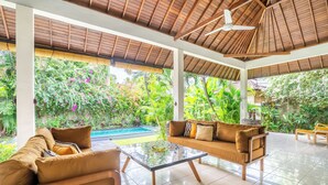A spacious indoor area with a glass coffee table, two sofas, and a ceiling fan. - Villa Amaro - 2 Bedrooms (Seminyak)