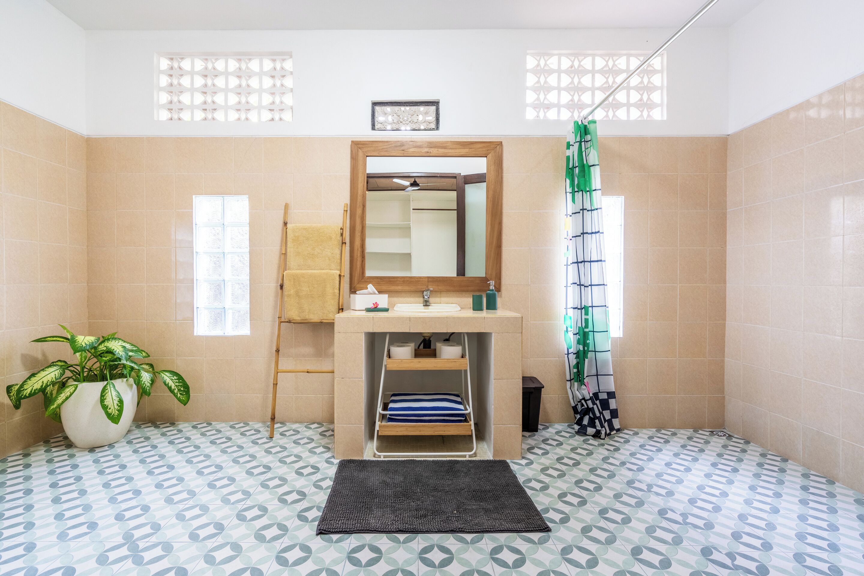 A bathroom with a sink, mirror, towel rack, potted plant, and patterned floor tiles.