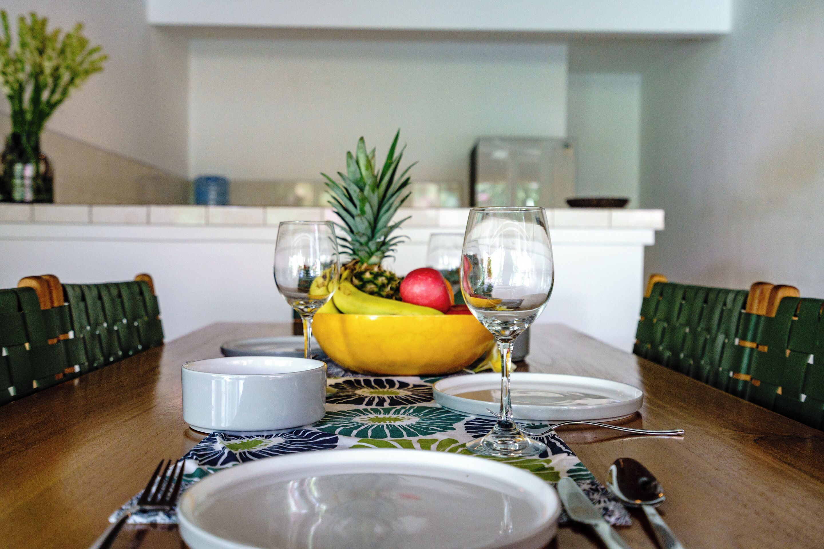 A dining table set with plates, cutlery, a fruit bowl, and wine glasses.
