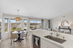 A modern kitchen with a large island, a dining area with chairs, and a view of the backyard. - Stay Close to The Beach at Marina's Sand Piper! (Marina)