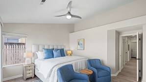 Ein Schlafzimmer mit einem Bett, zwei Stühlen, einem Nachttisch, einer Lampe, einem Deckenventilator und einem Fenster mit Jalousien.