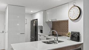 Een moderne keuken met witte kastjes, een roestvrijstalen spoelbak, een zwarte koelkast, een gasfornuis en een wandklok.