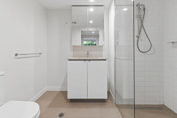 Un baño moderno con inodoro, lavamanos con espejo y cabina de ducha con vidrio.