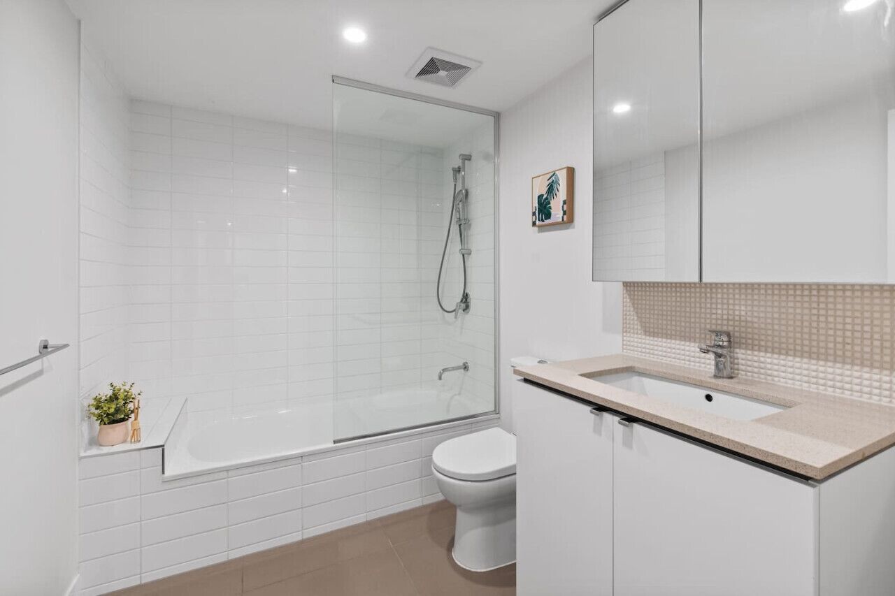 A modern bathroom with a glass-enclosed shower, a white toilet, and a sink with a beige countertop.