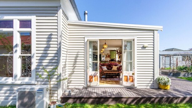 Une maison blanche avec une terrasse en bois, un climatiseur visible et un petit jardin.