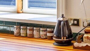 Une cuisine avec une fenêtre, une bouilloire et des pots d’épices sur le plan de travail.