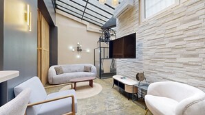 A modern living room with a sofa, chairs, a coffee table, and a TV mounted on a stone wall. - TBS 242 - Exceptional triplex loft (Paris)