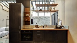A modern kitchen with dark cabinetry, a built-in oven, and a countertop with a kettle and toaster. There is a window above the sink and a skylight in the ceiling. - TBS 242 - Exceptional triplex loft (Paris)