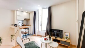 A compact living space with a kitchenette, a dining area, a seating area with a TV, and a small table with a bottle and glass.