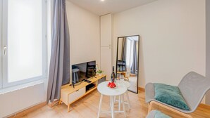 A modern living room with a TV, a small table with a wine glass, a chair, and a large mirror.