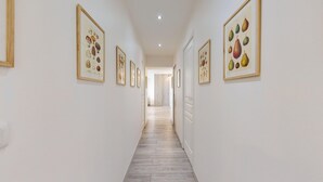A hallway with framed botanical prints on the walls, leading to a room with a wooden floor and a door.