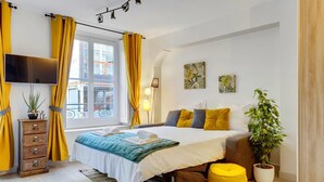 A modern bedroom with a bed, a TV, a dresser, and a window with yellow curtains.