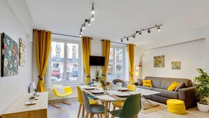 A modern living room with a dining area, yellow curtains, a grey sofa, and a flat-screen TV.
