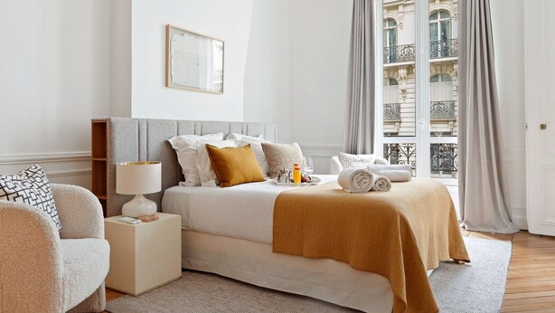 A hotel room with a bed, bedside table, lamp, and a view of a building through the window. - TheBlueStay 153 - Outstanding spacious suite - A/C (Paris)