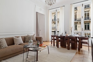 Una sala de estar con sofá, mesa de centro y comedor con sillas y una mesa dispuesta para una comida.