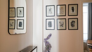 A hallway with framed artwork on the walls, a mirror, a vase with dried flowers, and a marble-topped console table. - TheBlueStay 153 - Outstanding spacious suite - A/C (Paris)