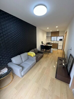Uma sala de estar moderna com um sofá cinzento, uma pequena mesa lateral e uma parede escura.