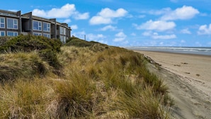 Ein Küstengebäude mit sandigem Strand und grasbewachsenen Dünen im Vordergrund.