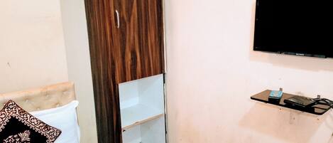 A bedroom with a wardrobe, a bed, a bedside table, a TV, and a small shelf.