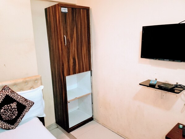 Une chambre comprenant une armoire, un lit, une table de chevet, un téléviseur et une petite étagère.