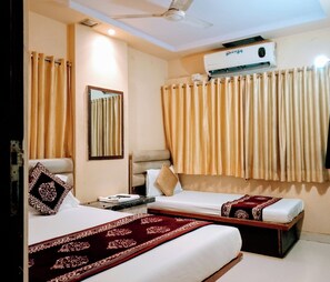 A hotel room with two beds, a ceiling fan, an air conditioning unit, and a window with curtains. - Hotel Talon (Mumbai)