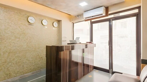 A reception area with a wooden reception desk, a clock, and an air conditioning unit. - Hotel Talon (Mumbai)