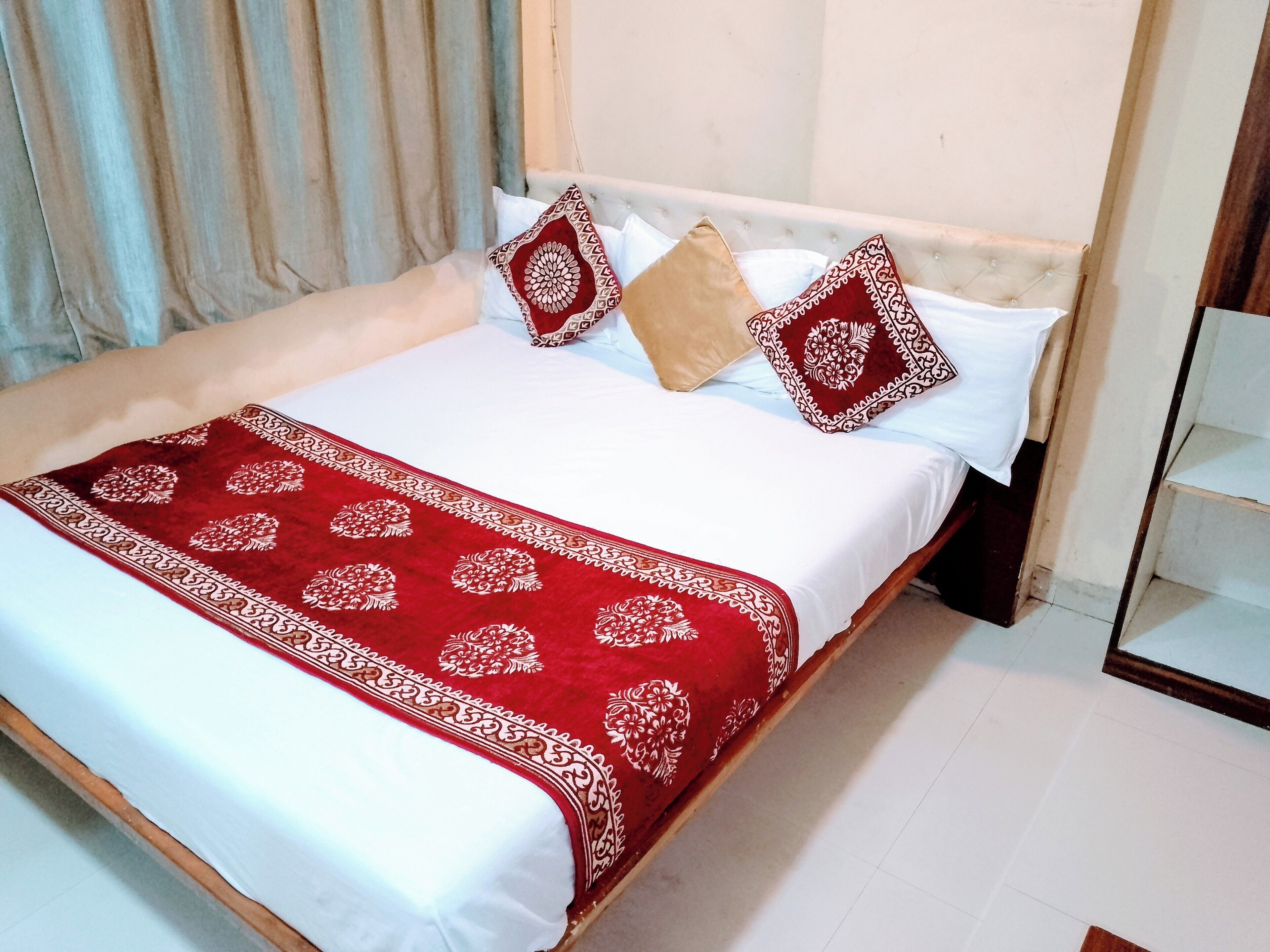 A neatly made bed with a red and white patterned bedspread, two pillows with a red and white design, and a wooden headboard.