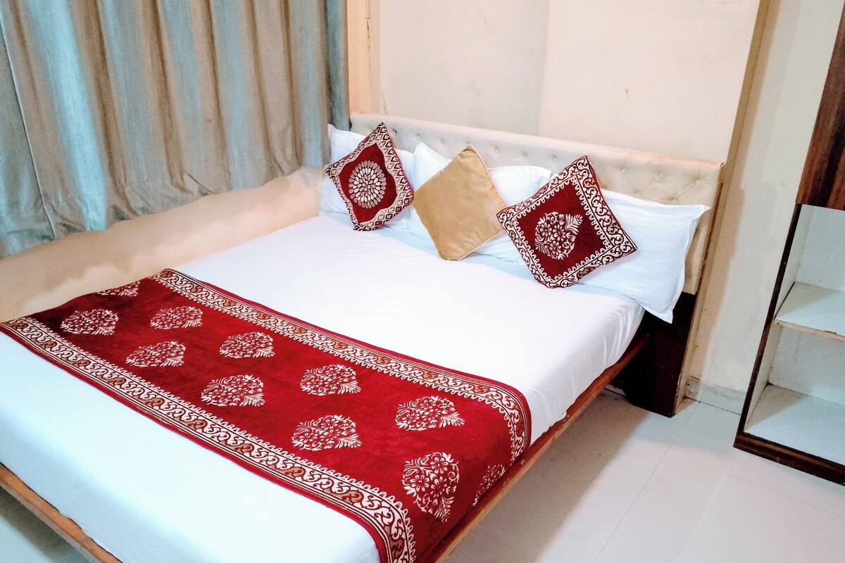 A neatly made bed with a red and white patterned bedspread, two pillows with a red and white design, and a wooden headboard.