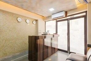 Un espace d’accueil comprenant un comptoir de réception en bois, une horloge et un appareil de climatisation.