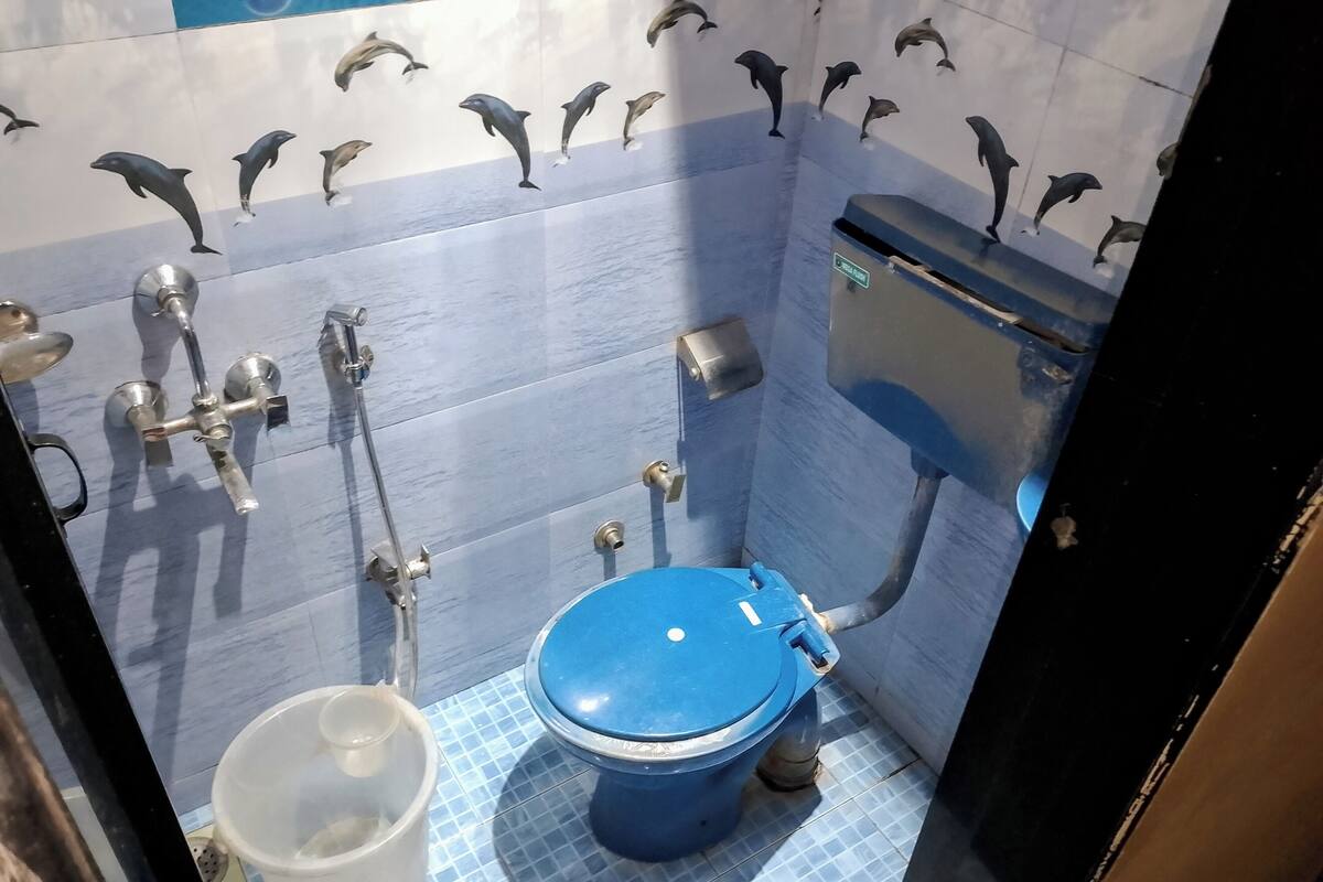 A bathroom with a blue toilet, a handwashing station, and a trash bin.