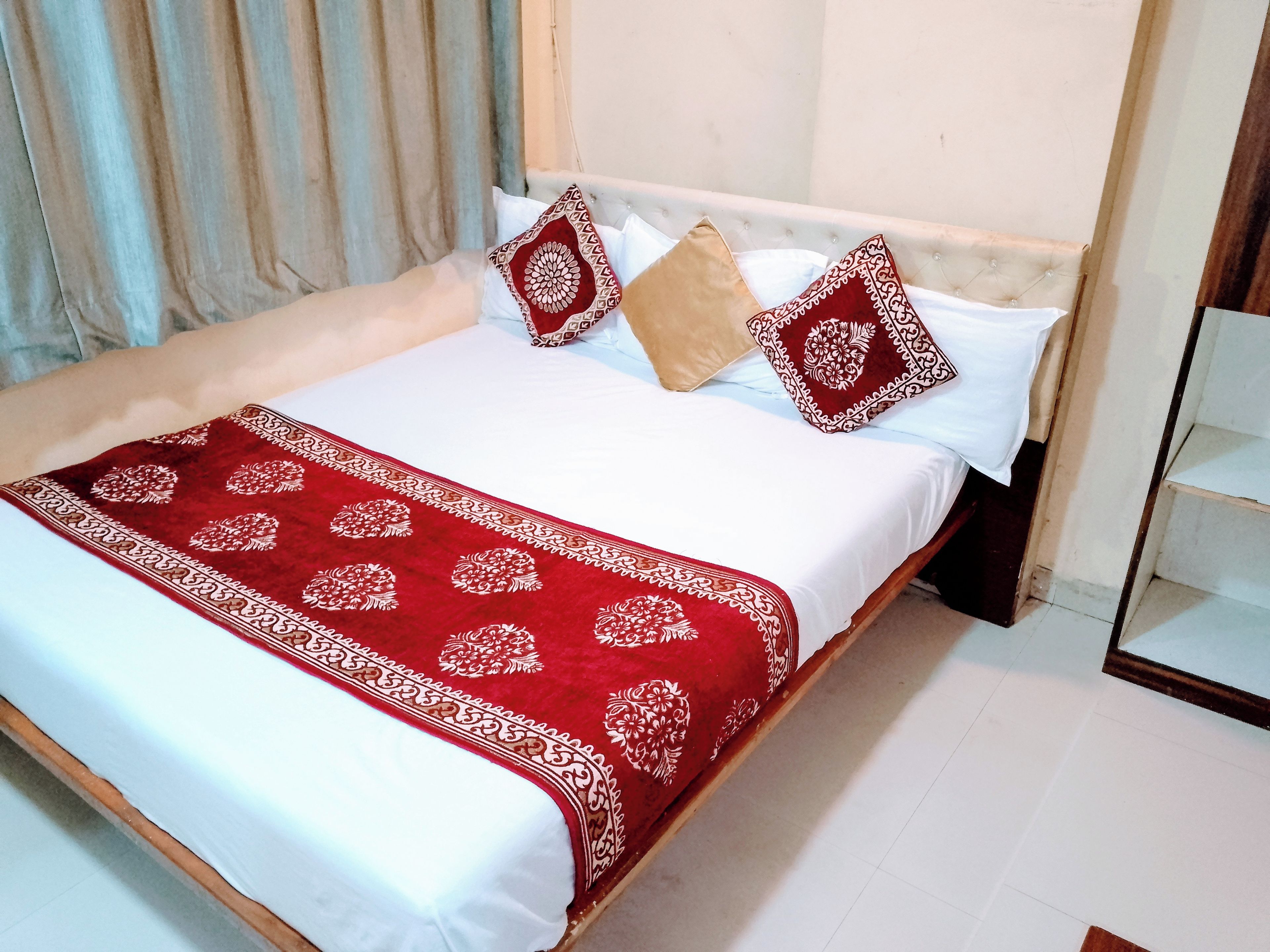 A neatly made bed with a white and red bedspread, two patterned pillows, and a red decorative throw.