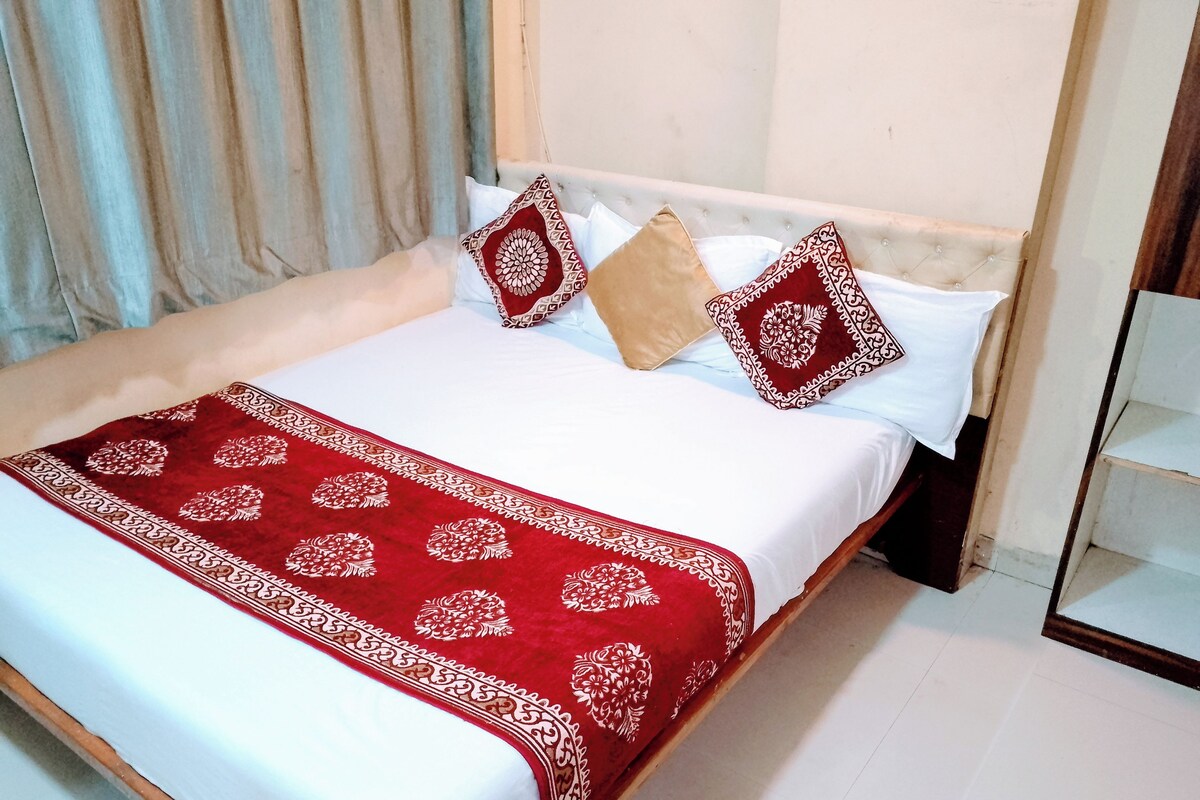 Un lit bien fait, recouvert d’une couvre-lit blanche et rouge, agrémenté de deux coussins à motifs et d’un plaid décoratif rouge.