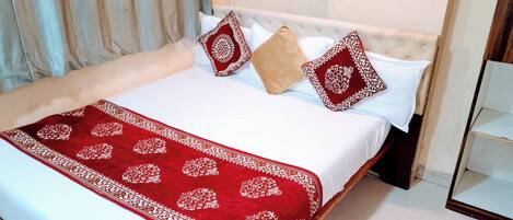 A neatly made bed with a white and red bedspread, two patterned pillows, and a red decorative throw.
