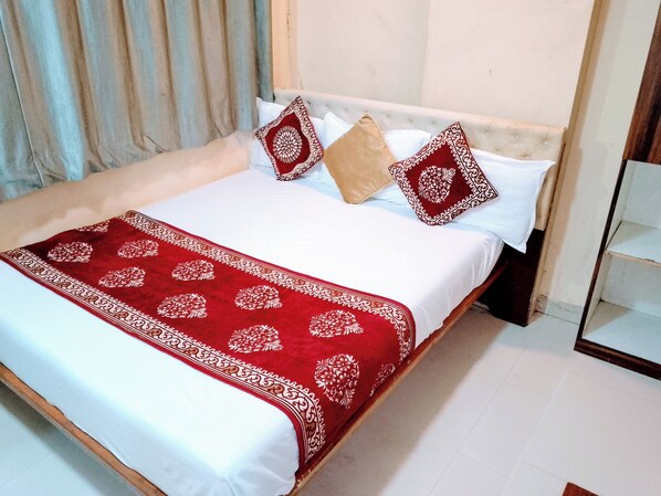 A neatly made bed with a white and red bedspread, two patterned pillows, and a red decorative throw. - Hotel Talon (Mumbai)