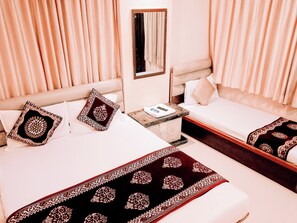 Une chambre d’hôtel avec deux lits, chacun recouvert d’une couvre-lit à motifs et agrémenté d’oreillers assortis. On y trouve une petite table de chevet avec une télécommande et un miroir au-dessus.