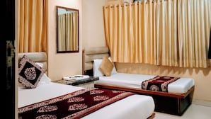A hotel room with two beds, a ceiling fan, an air conditioning unit, and a window with curtains. - Hotel Talon (Mumbai)