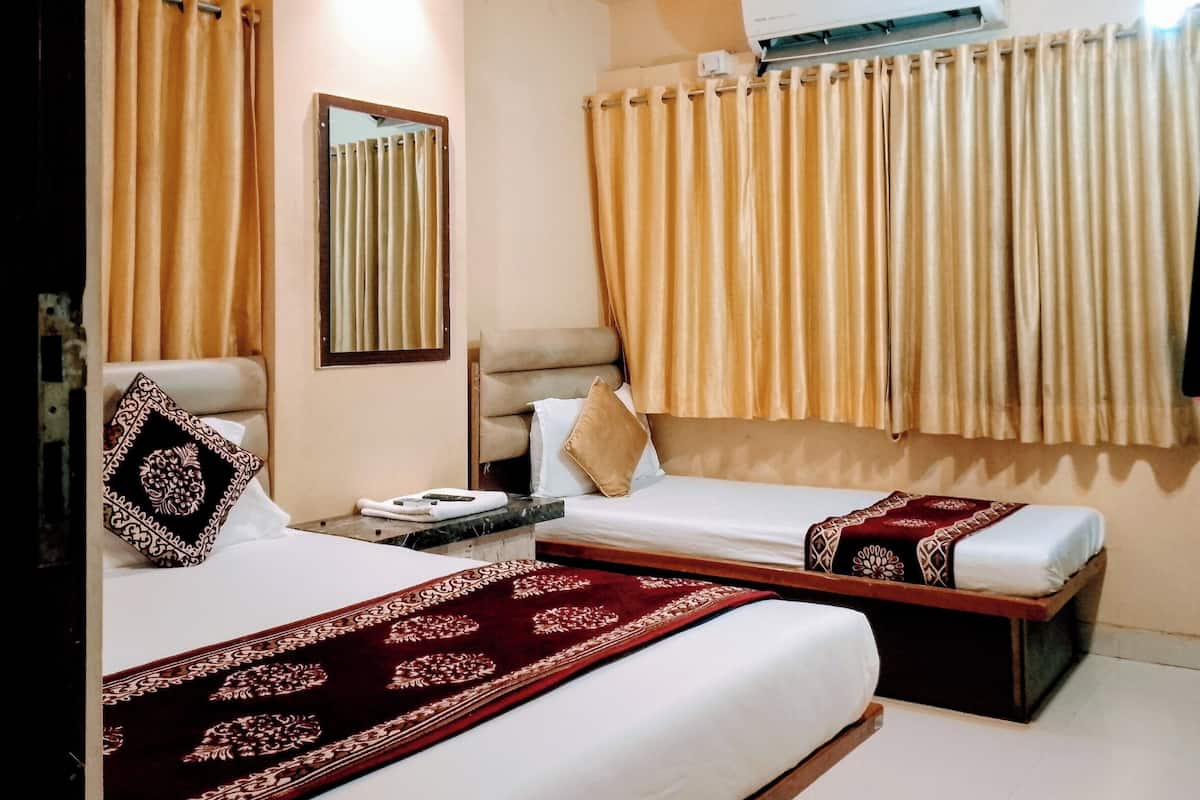 A hotel room with two beds, a ceiling fan, an air conditioning unit, and a window with curtains.